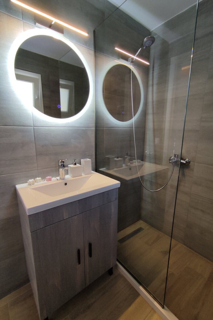 Nemertes' modern bathroom with grey tiles, a shower and a sink with a mirror.