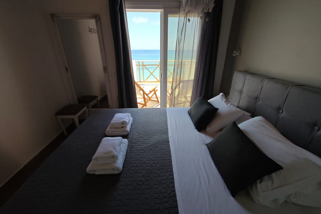 The double bed with grey linen and fresh white towels on top in Nemertes' bedroom.
