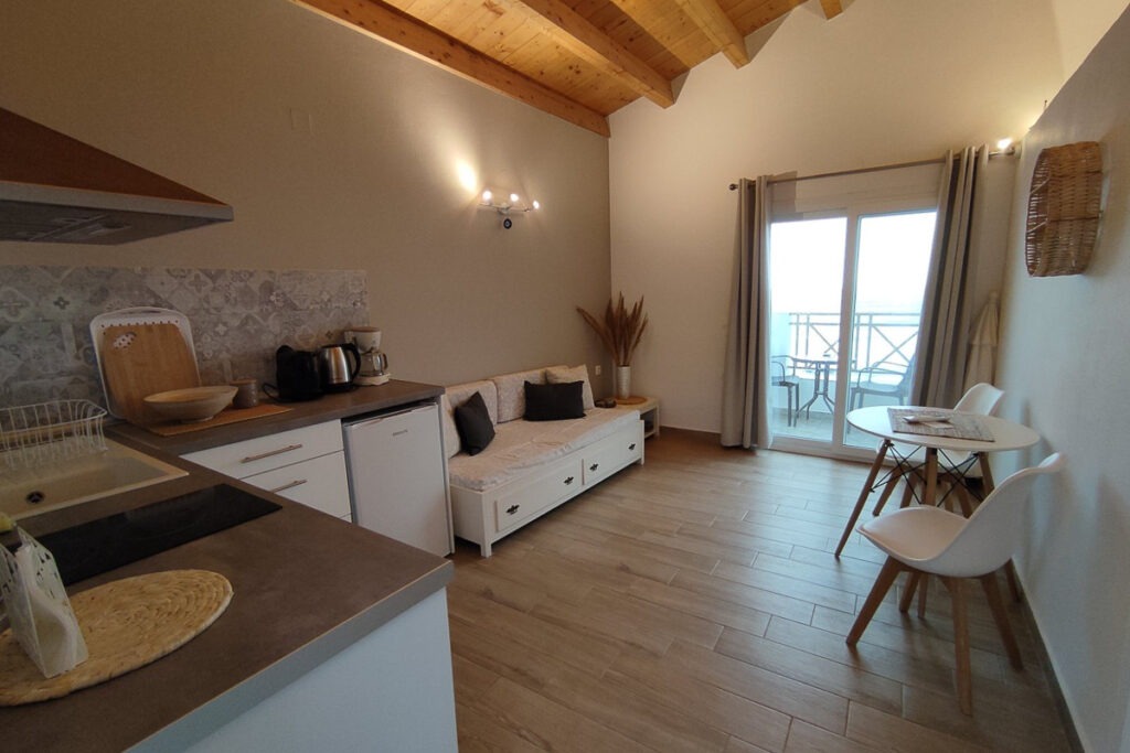 The spacious living room and kitchenette area of Nemertes studio equipped with a white sofa, a white round table with two chairs and a small fridge.
