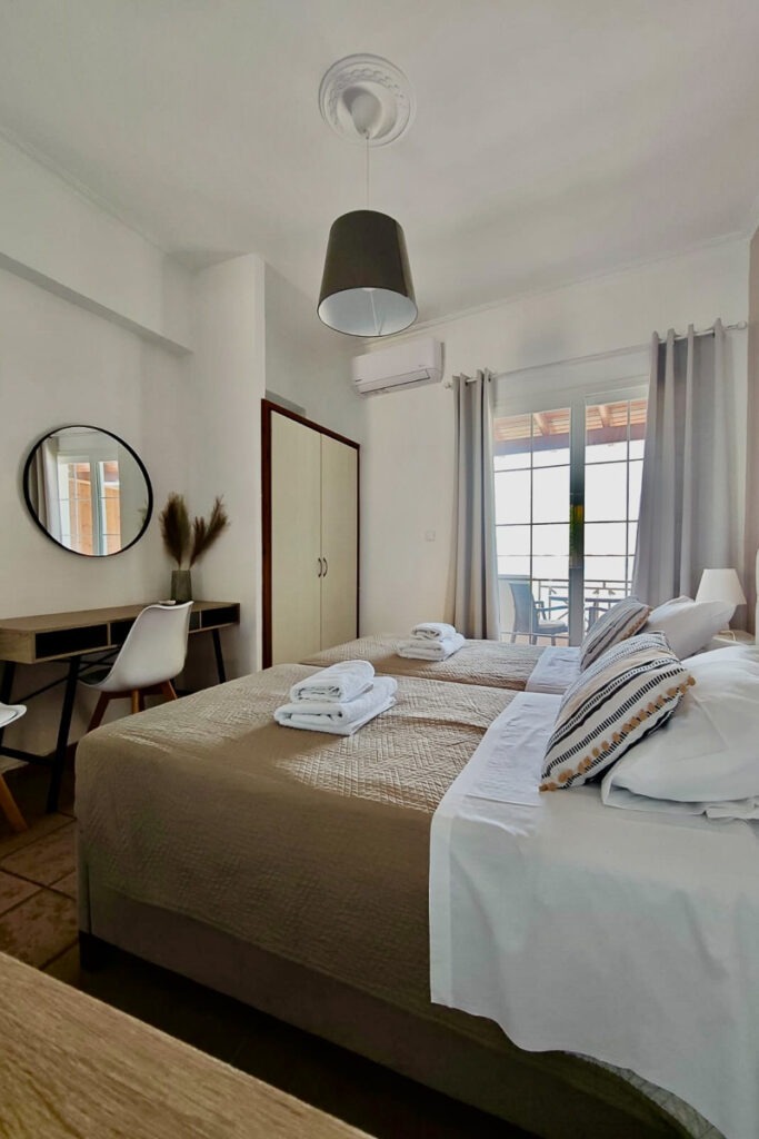 Two large beds next to each other in Cymatologe studio. Across the beds is a small desk with a chair and a small closet.