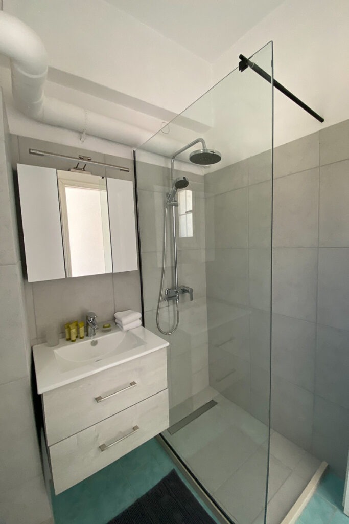 Glafki's modern bathroom with grey tiles, a shower and a sink with a mirror.