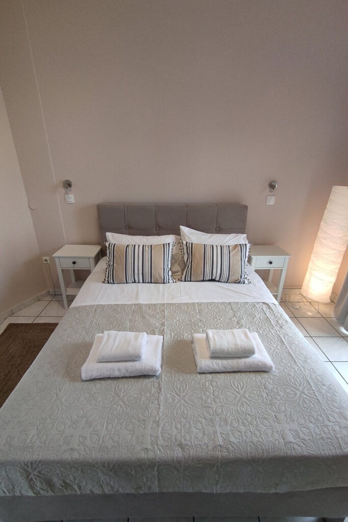 The double bed of melite studio. It has grey linen and two bedside tables.