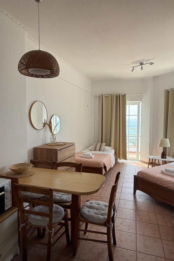 Pasithea's apartment living room. There's a kitchen table with three chairs and two single beds-sofas.