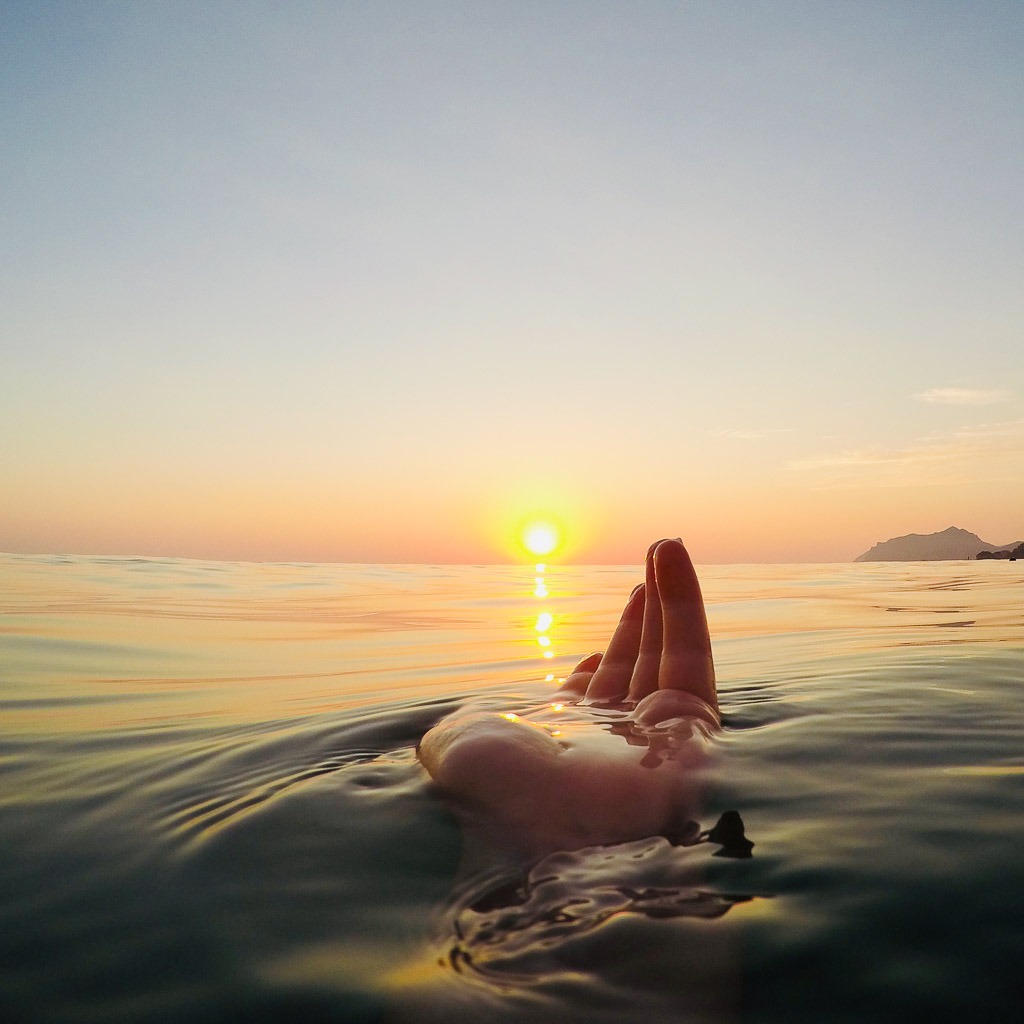 The palm of a hand in the sea water with the sunset in the background.